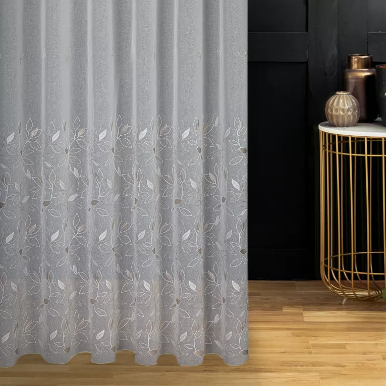 Firana szyta na tunelu kremowo beżowa z matowej etaminy haftowanej w roślinny wzór z połyskującą nicią, wykończona obciążnikiem